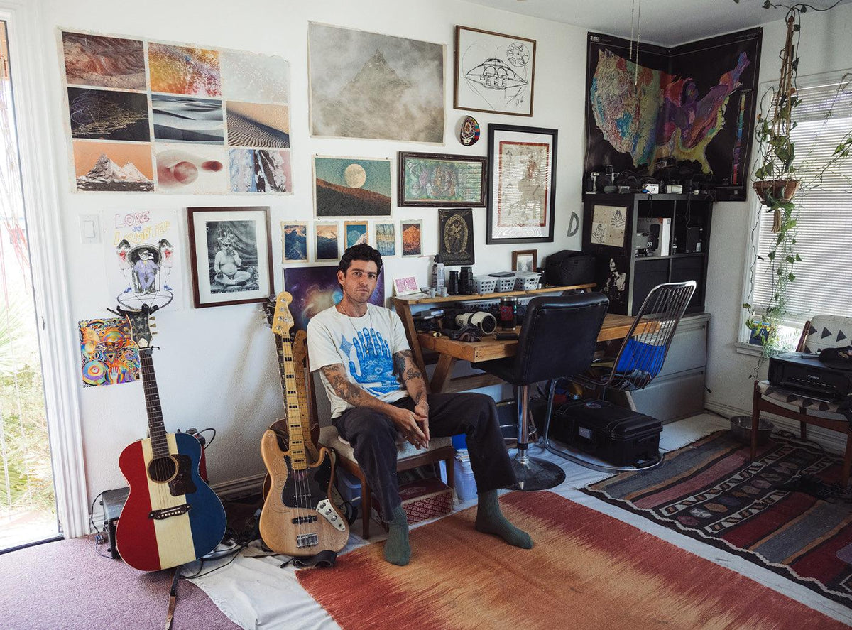 Brian Merriam seated beside guitars in a studio filled with photographs and artwork