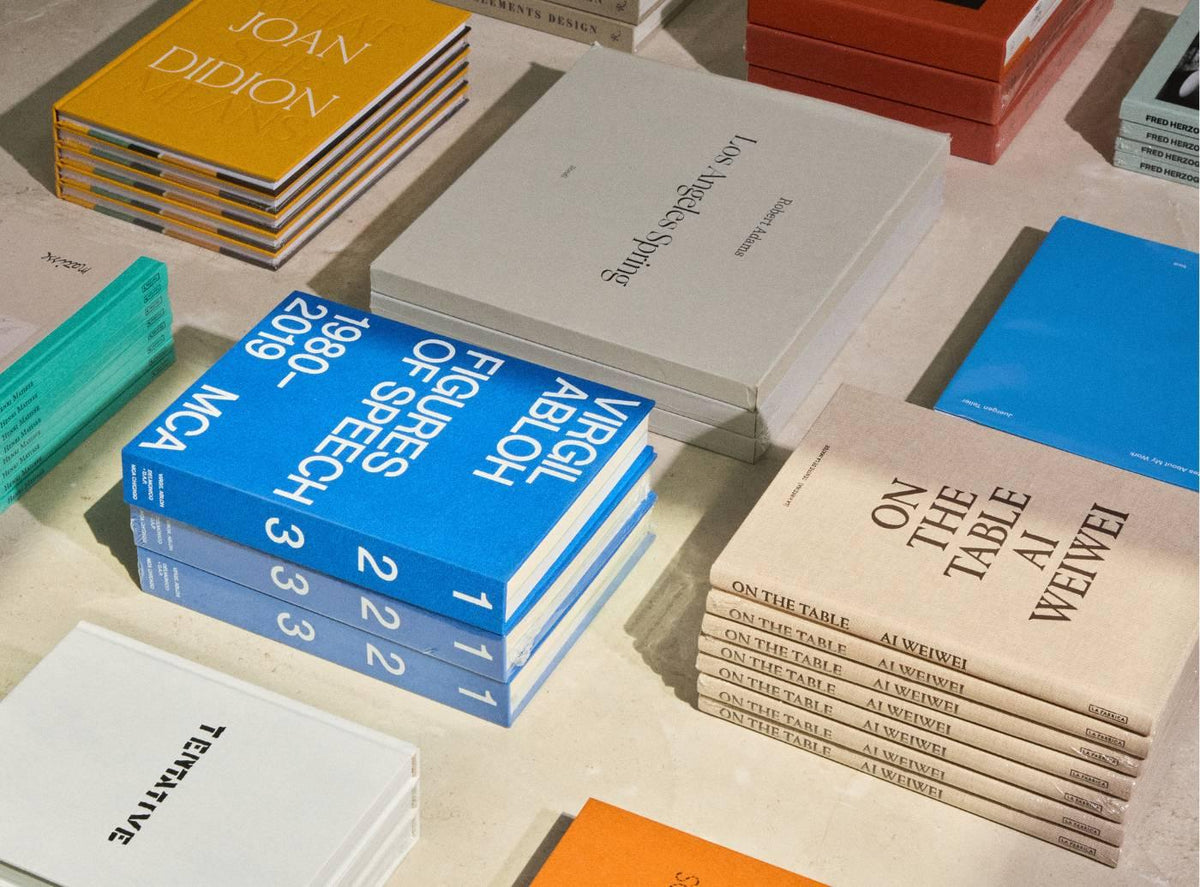 Selection of hardcover books in varied colors including yellow blue and tan arranged on a light stone surface