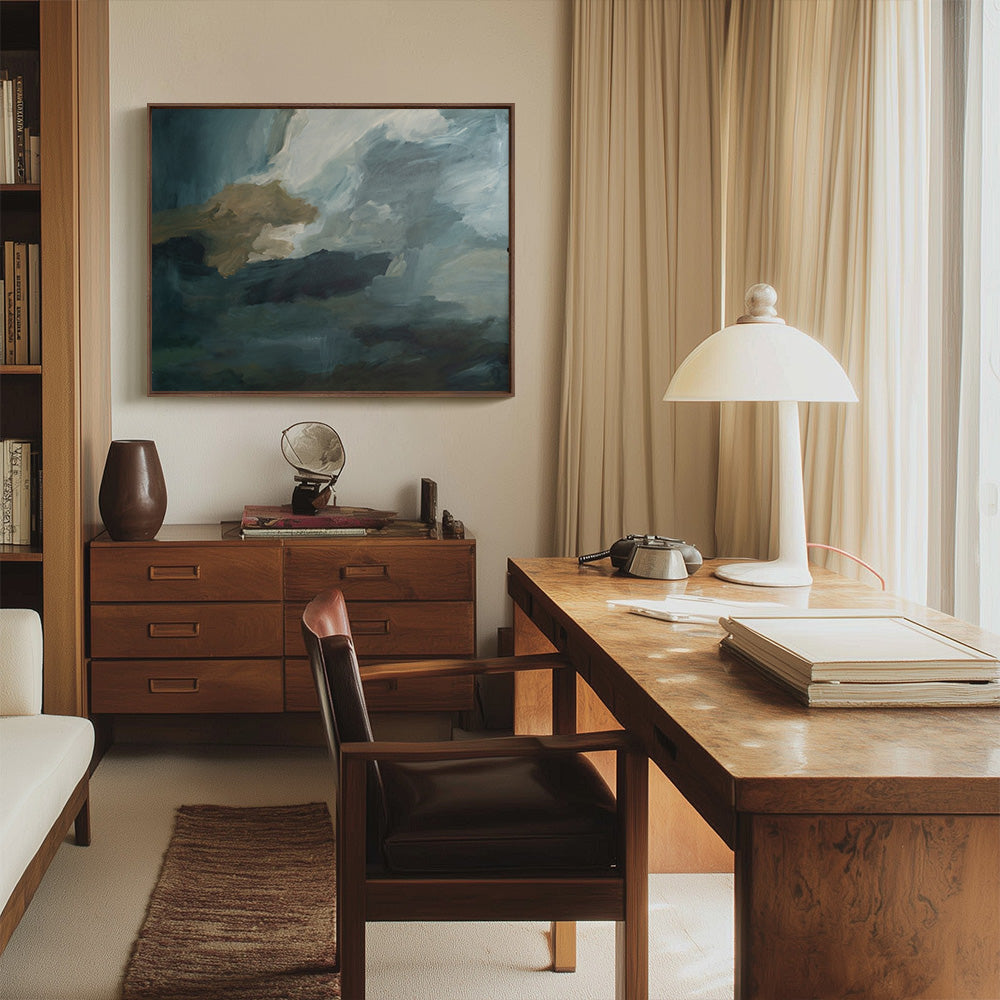 A painting with dark blue white and brown brushstrokes hangs above a wooden credenza in a sunlit office