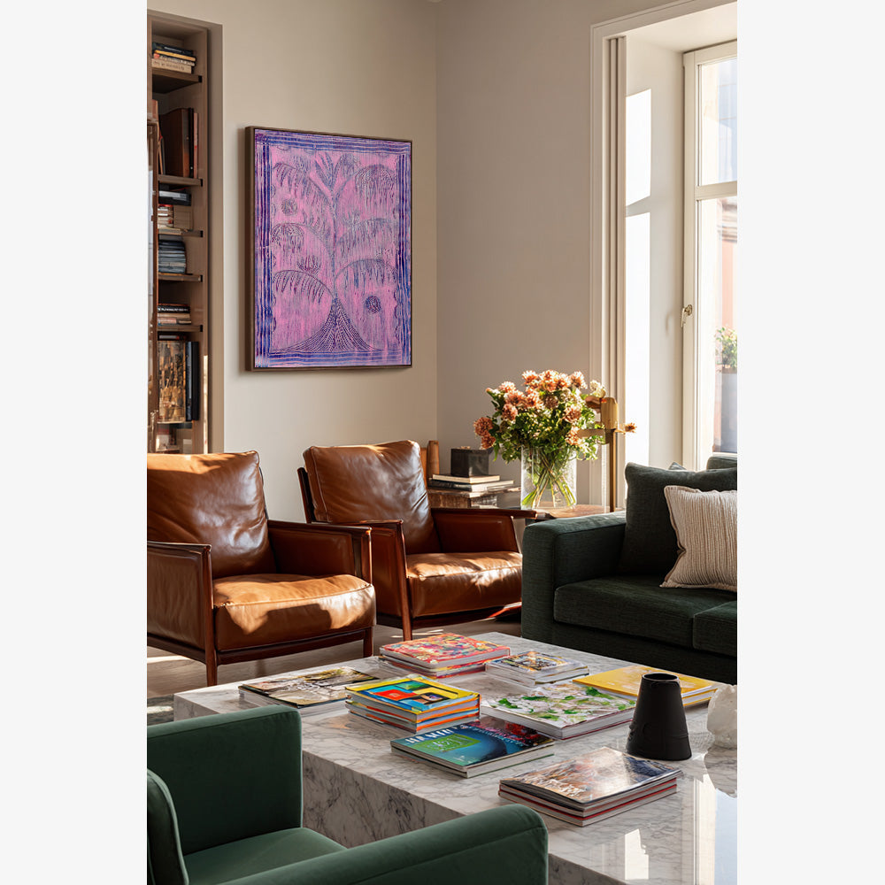 A pink and purple abstract painting with palm tree motifs hangs above two brown leather armchairs