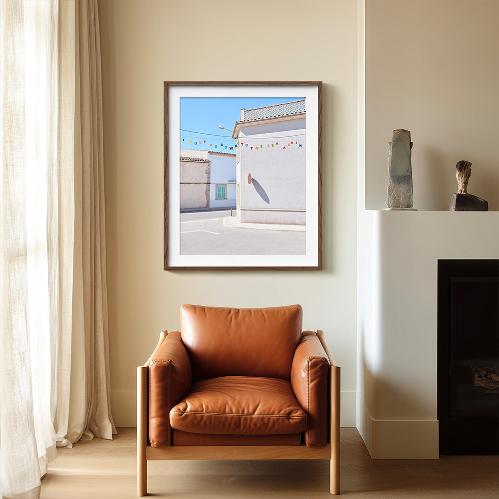 Down to the Sea print in a brown frame displayed above a brown leather armchair next to a fireplace