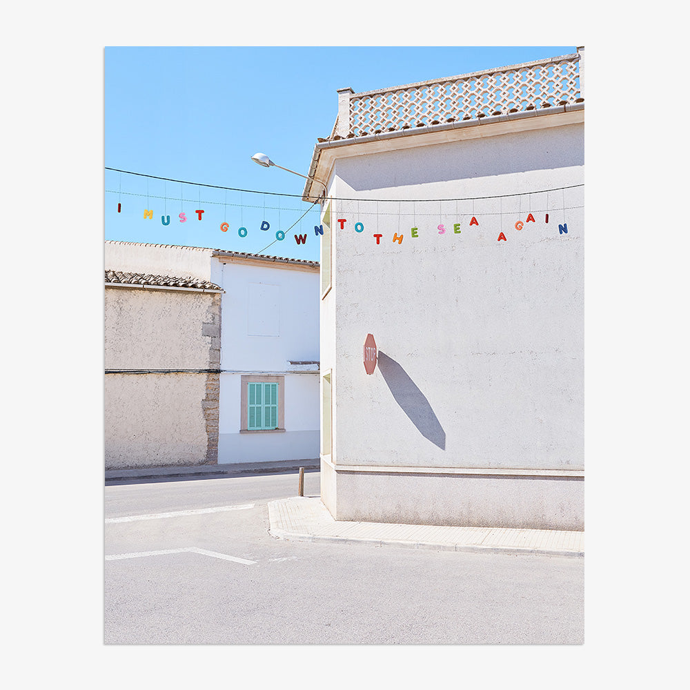 Colorful letters on a string spelling I MUST GO DOWN TO THE SEA AGAIN hung across a white building