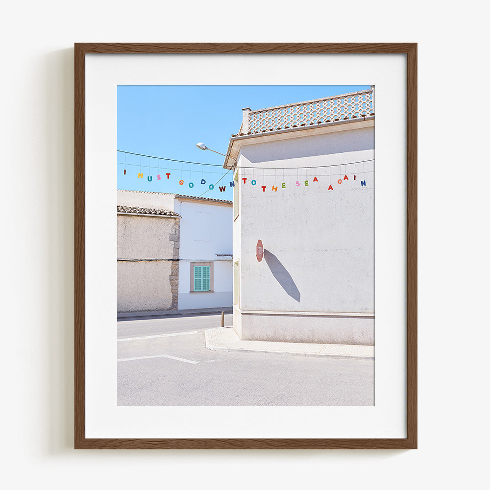 Close-up vertical photo print featuring white stucco buildings with a green shutter and colorful bunting framed in dark