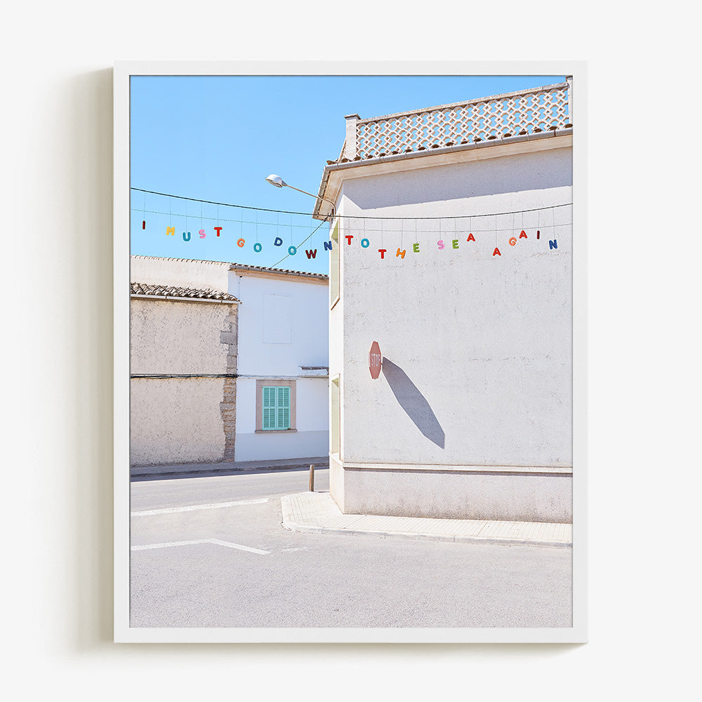 Vertical photo print featuring white stucco buildings with a green shutter and colorful bunting framed in white