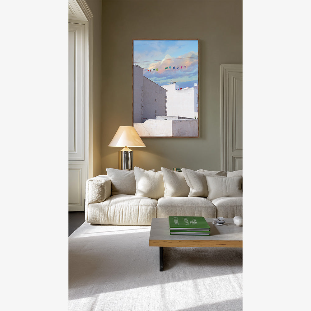 Like Wonder print in a living room White buildings blue and pink sky and LIKE WONDER in colorful letters A white couch