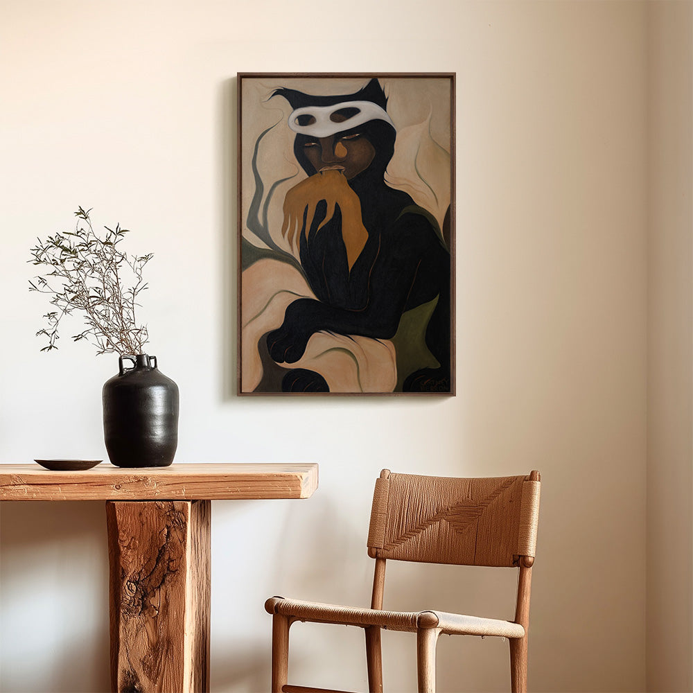 Framed vertical painting of a dark stylized figure with a white mask hanging on a wall above a wooden table