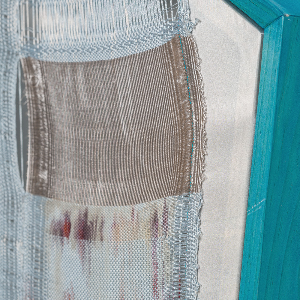 Close-up of a blue and white woven textile within a bright teal wooden frame showing frayed edges