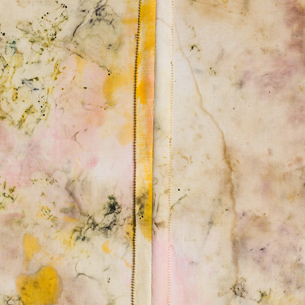 Close-up of a textile with organic beige and pink stains and a central vertical seam with yellow pigment detail
