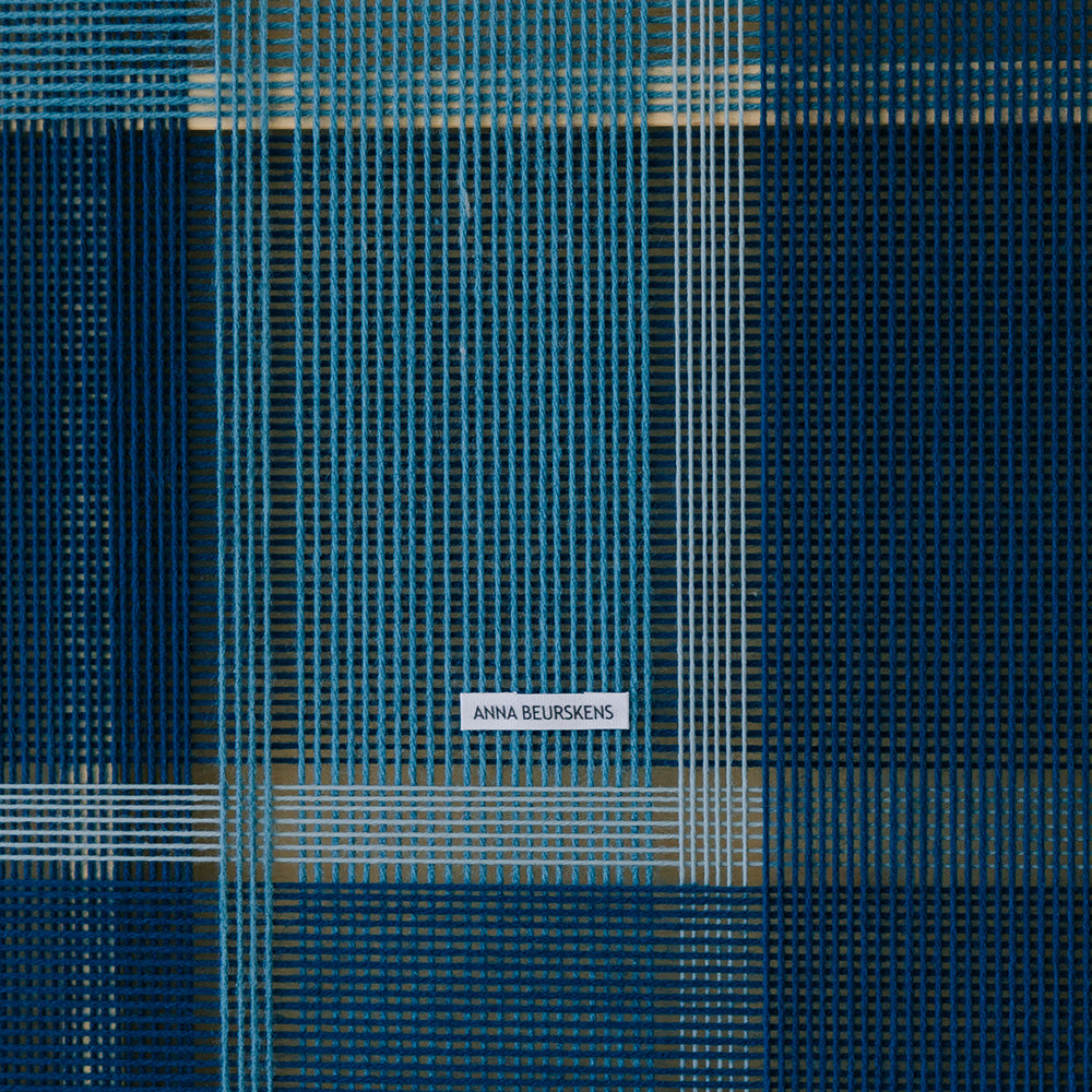 Close-up of textile art with blue and white threads a grid pattern and the artists label