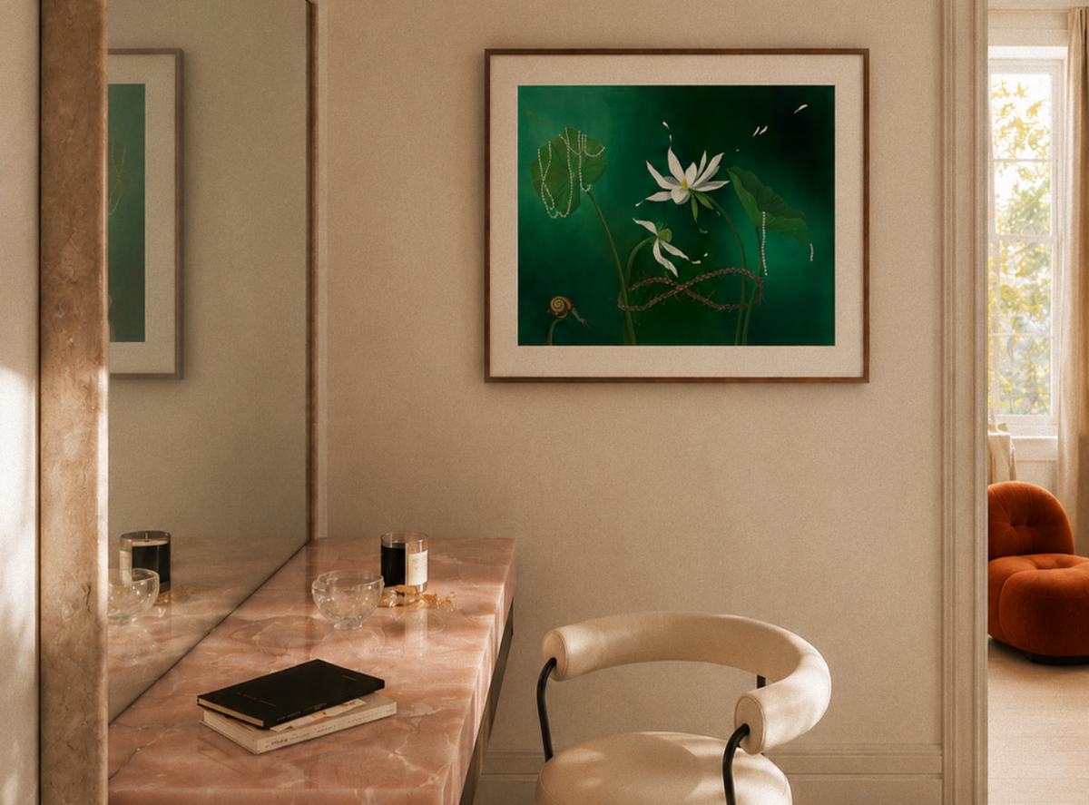 A framed art print featuring a green water lily painting hangs on a beige wall in a modern, sunlit room with a marble vanity desk and a cream-colored chair.