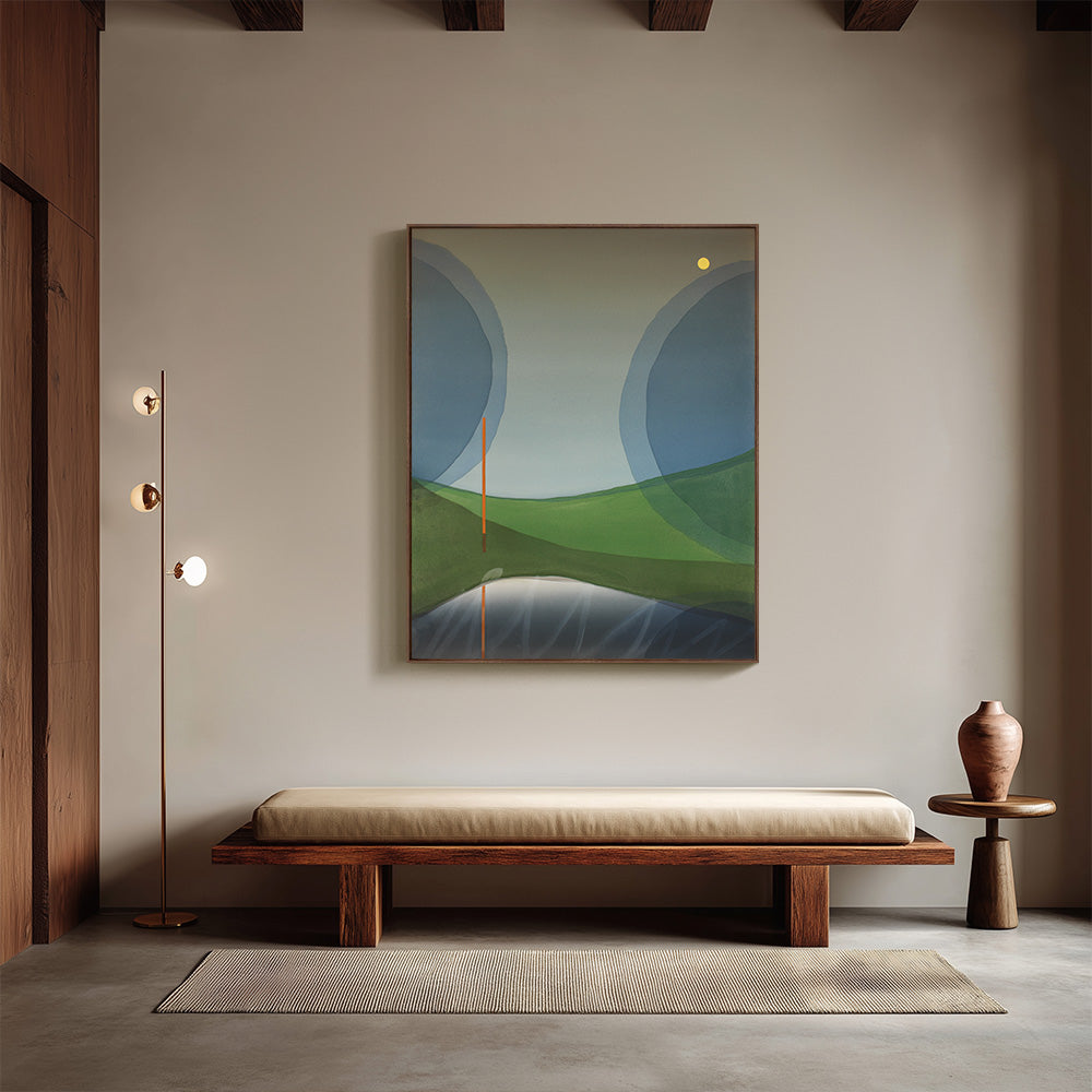 Framed painting of a minimalist landscape hanging in a neutral room above a long wooden bench and floor lamp