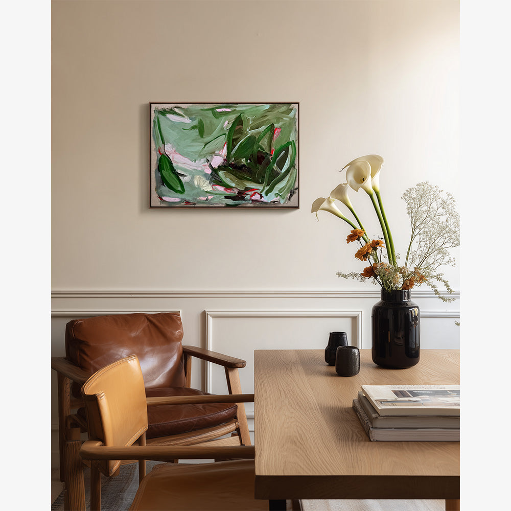A small abstract landscape painting hangs on a beige wall above a dining table with a vase of white calla lilies