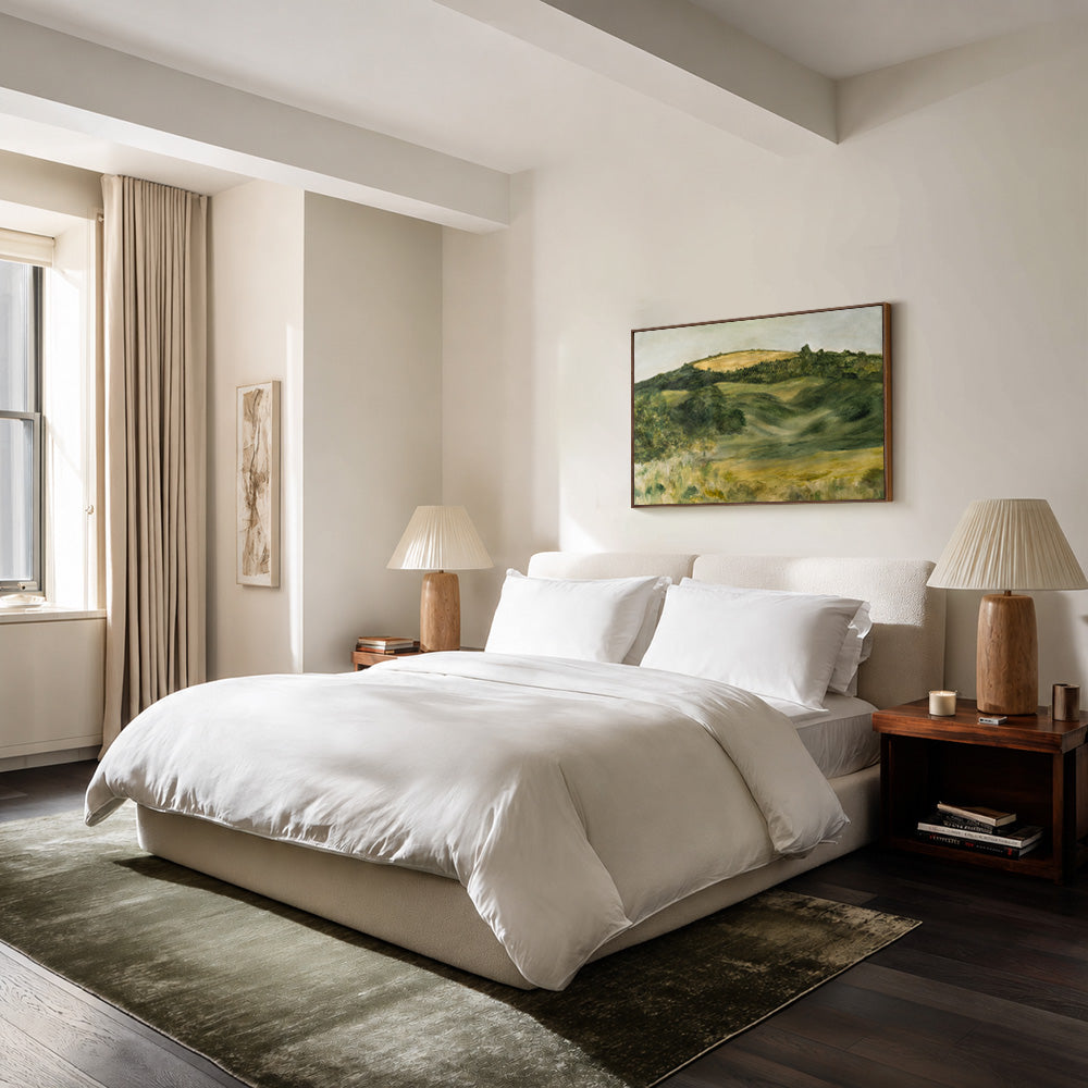 Bedroom with a painting of an Italian countryside above the bed two lamps and a window with light-colored curtains