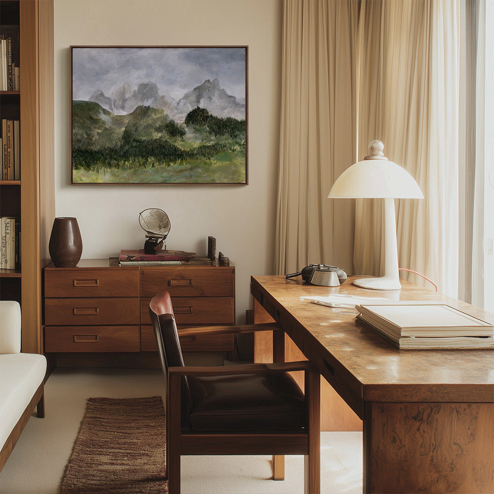 Painting of misty green mountains and forest hangs above a wooden desk in a well-lit office