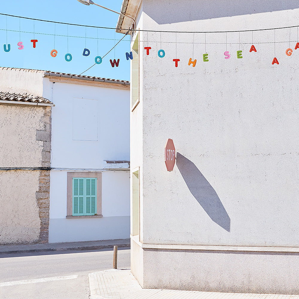A close-up of a print showing a white building with a stop sign shadow and colorful letters spelling I MUST GO DOWN TO