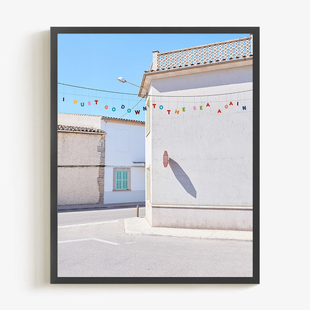 Coastal village photo print with white buildings colorful bunting and a sunlit street in a black frame