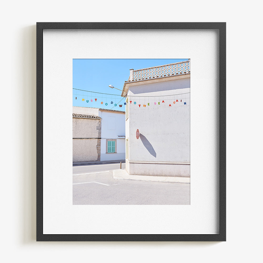 A framed print with a white border showing a white building with a stop sign shadow and colorful letters spelling I