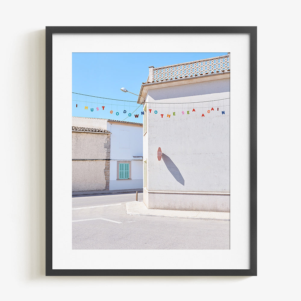 Close-up of a coastal village photo print with white buildings colorful bunting and a sunlit street in a black frame