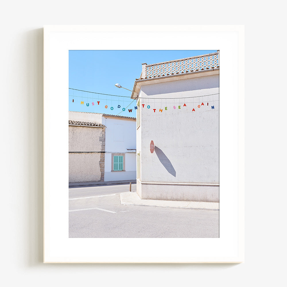 Coastal village photo print with white buildings colorful bunting and a sunlit street in a white frame