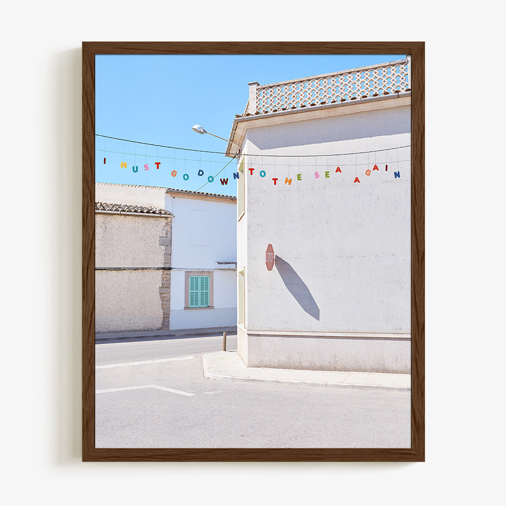 A dark wood framed print of a white building with a stop sign shadow and colorful letters spelling I MUST GO DOWN TO