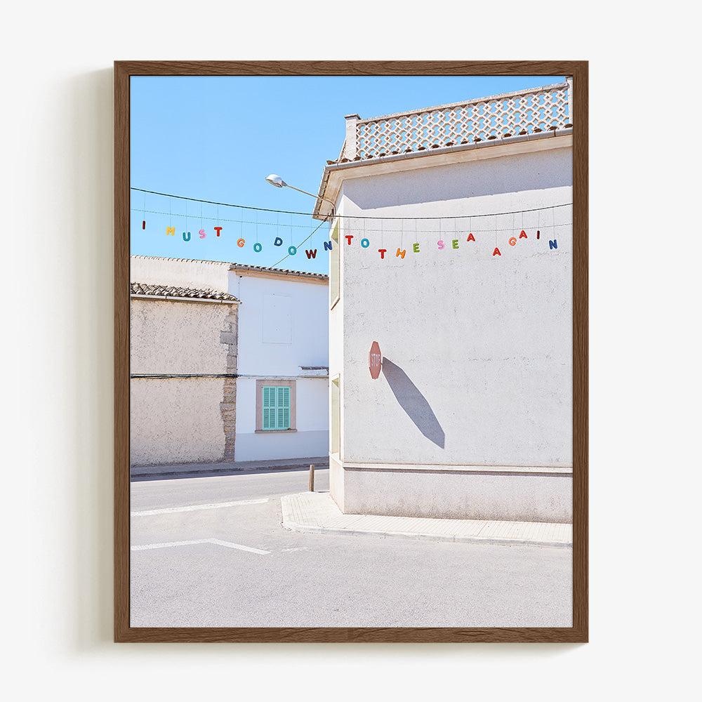 Vertical photo print featuring white stucco buildings with a green shutter and colorful bunting framed in dark wood