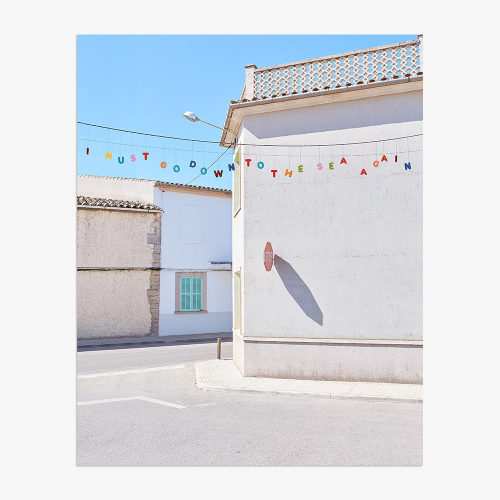 A print of a white building with a stop sign shadow and colorful letters spelling I MUST GO DOWN TO THE SEA AGAIN