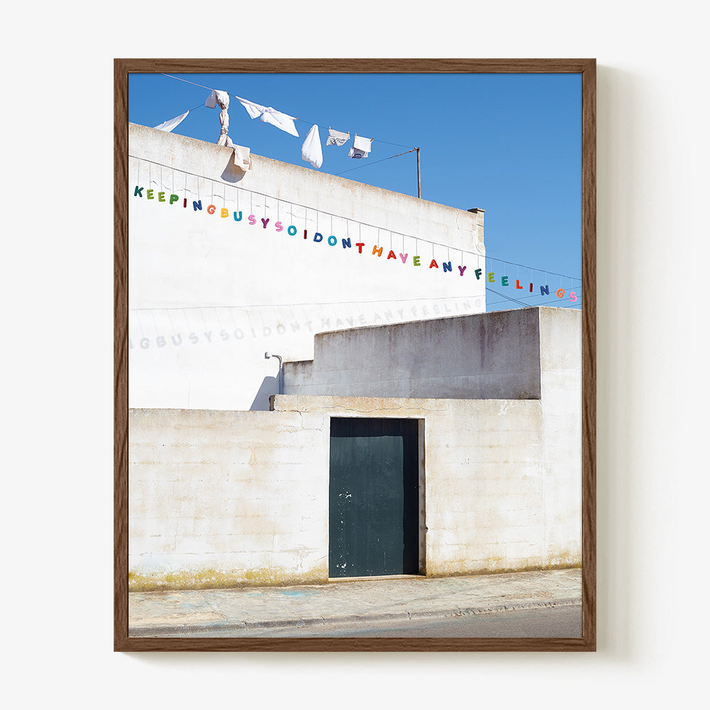 A print of a white building with colorful text bunting displayed in a dark brown wooden frame