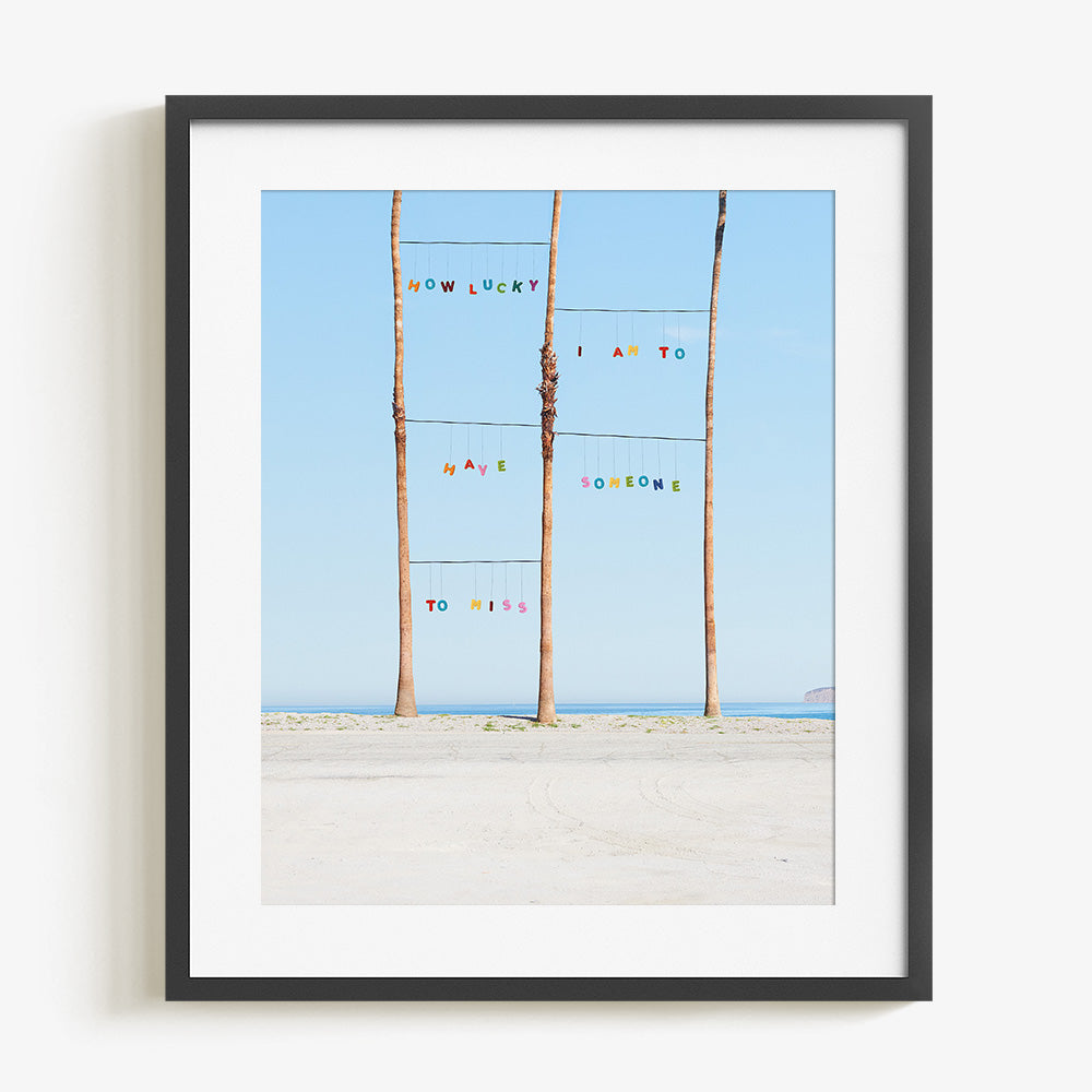 Framed print of three palm trees on a beach with the ocean in the background text reading HOW LUCKY I AM TO HAVE