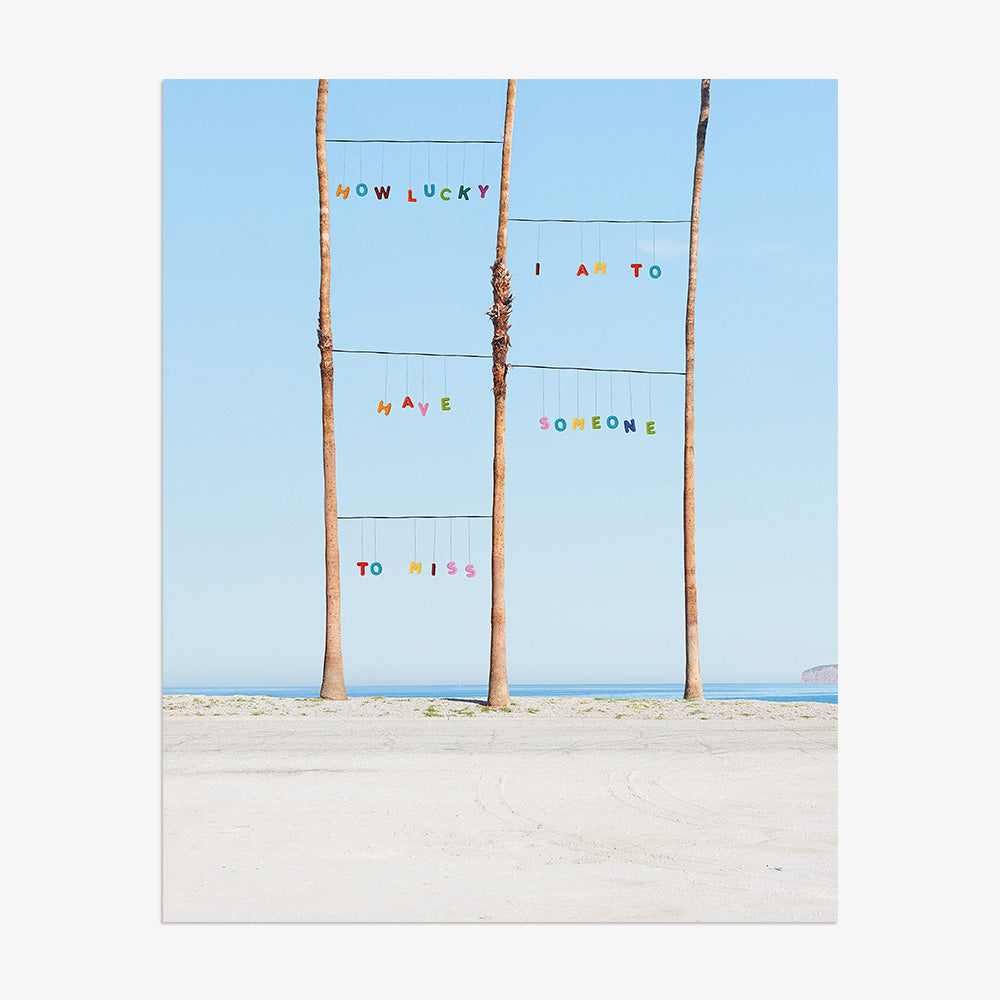 Lucky print by James Needham Colorful letters suspended between palm trees on a beach without a frame