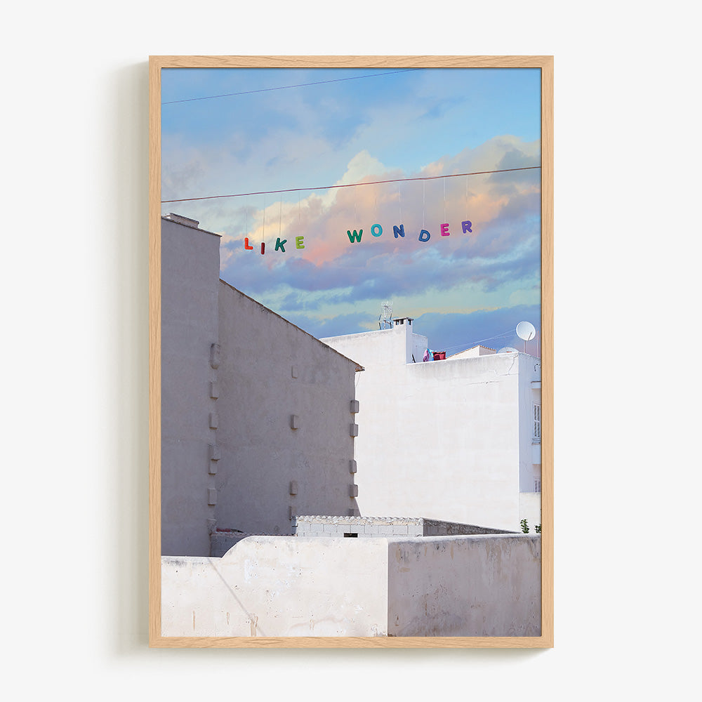 Like Wonder print by James Needham in a natural wood frame White buildings under a blue and pink cloudy sky with LIKE