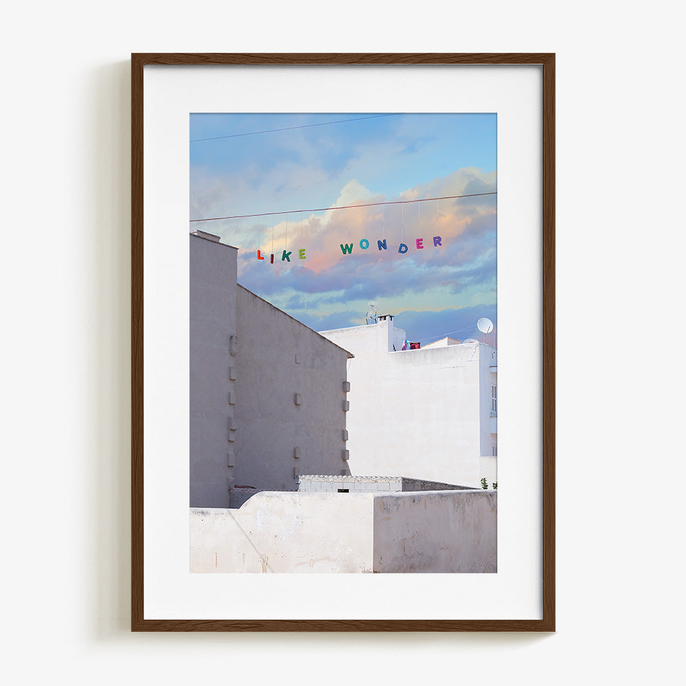 Like Wonder print by James Needham in a dark wood frame White buildings below a blue and pink cloudy sky with LIKE
