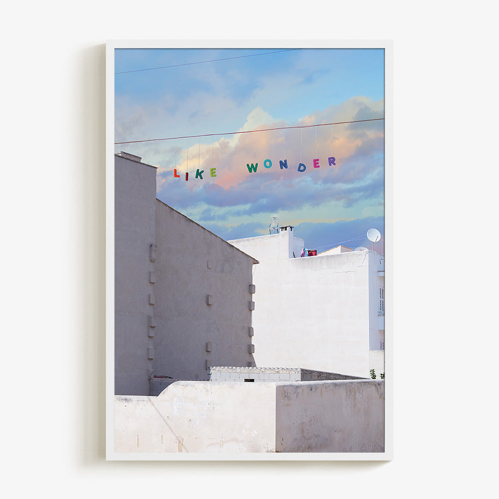 Like Wonder print by James Needham in a white frame White buildings under a blue and pink cloudy sky with LIKE WONDER