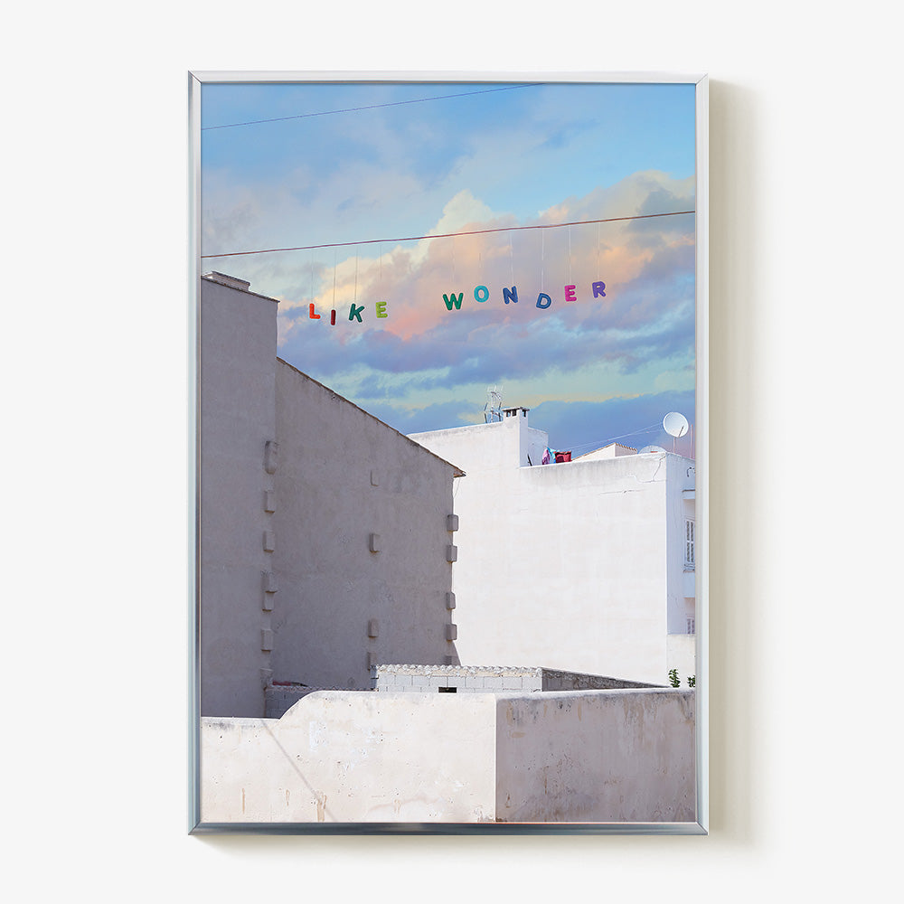 Like Wonder print by James Needham White buildings below a blue and pink cloudy sky with LIKE WONDER spelled in