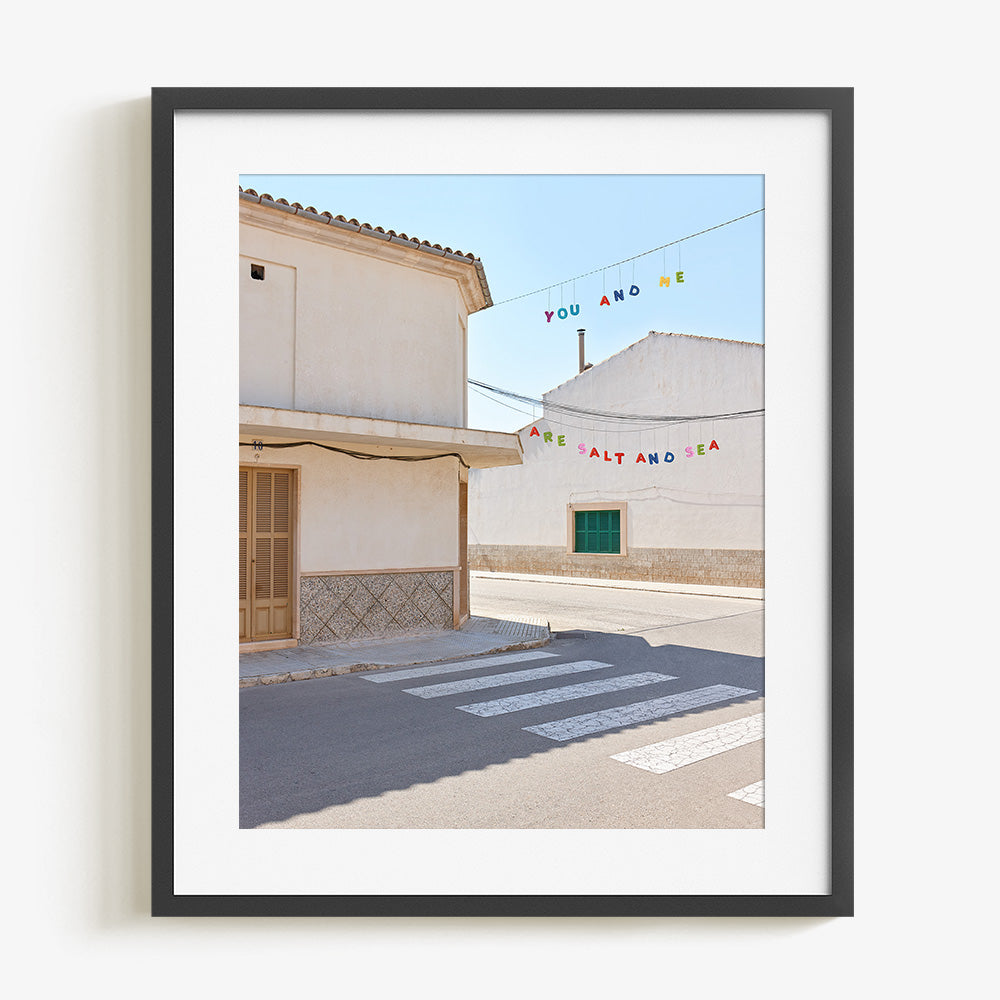 Street scene with white buildings a crosswalk and colorful hanging text in a charcoal frame