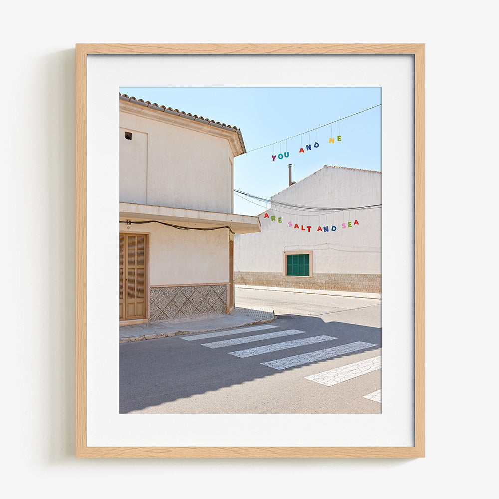 Street scene with white buildings a crosswalk and colorful hanging text in a natural wood frame