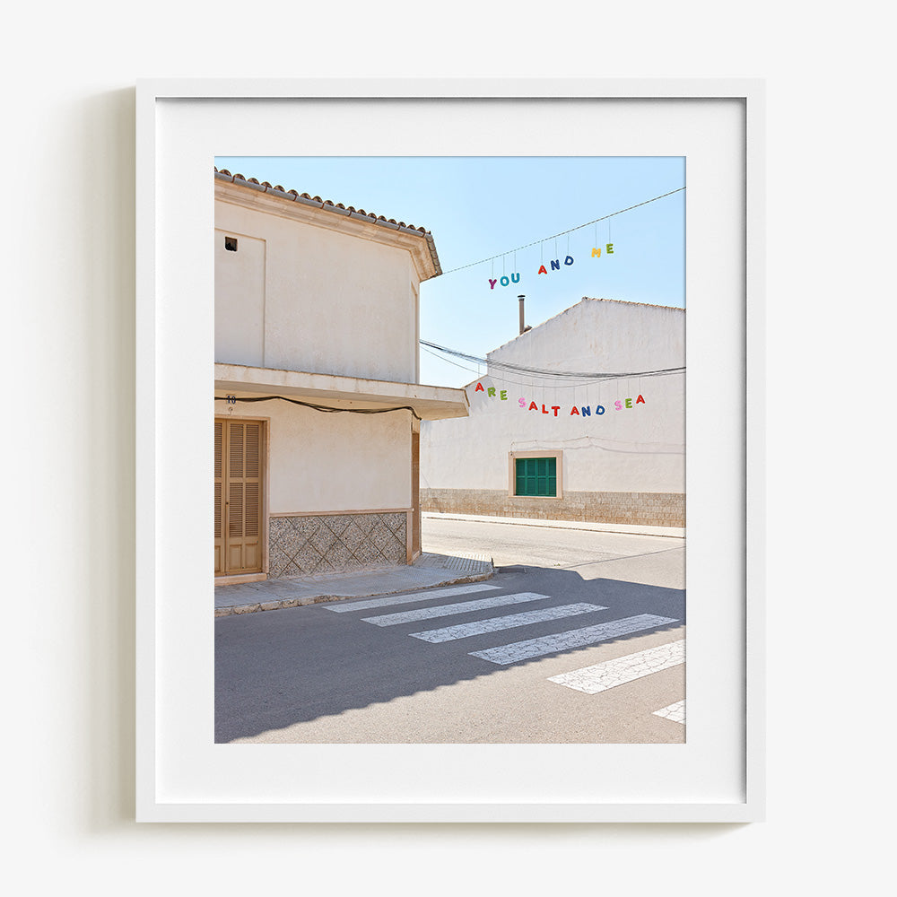 Street scene with white buildings a crosswalk and colorful hanging text in a white frame
