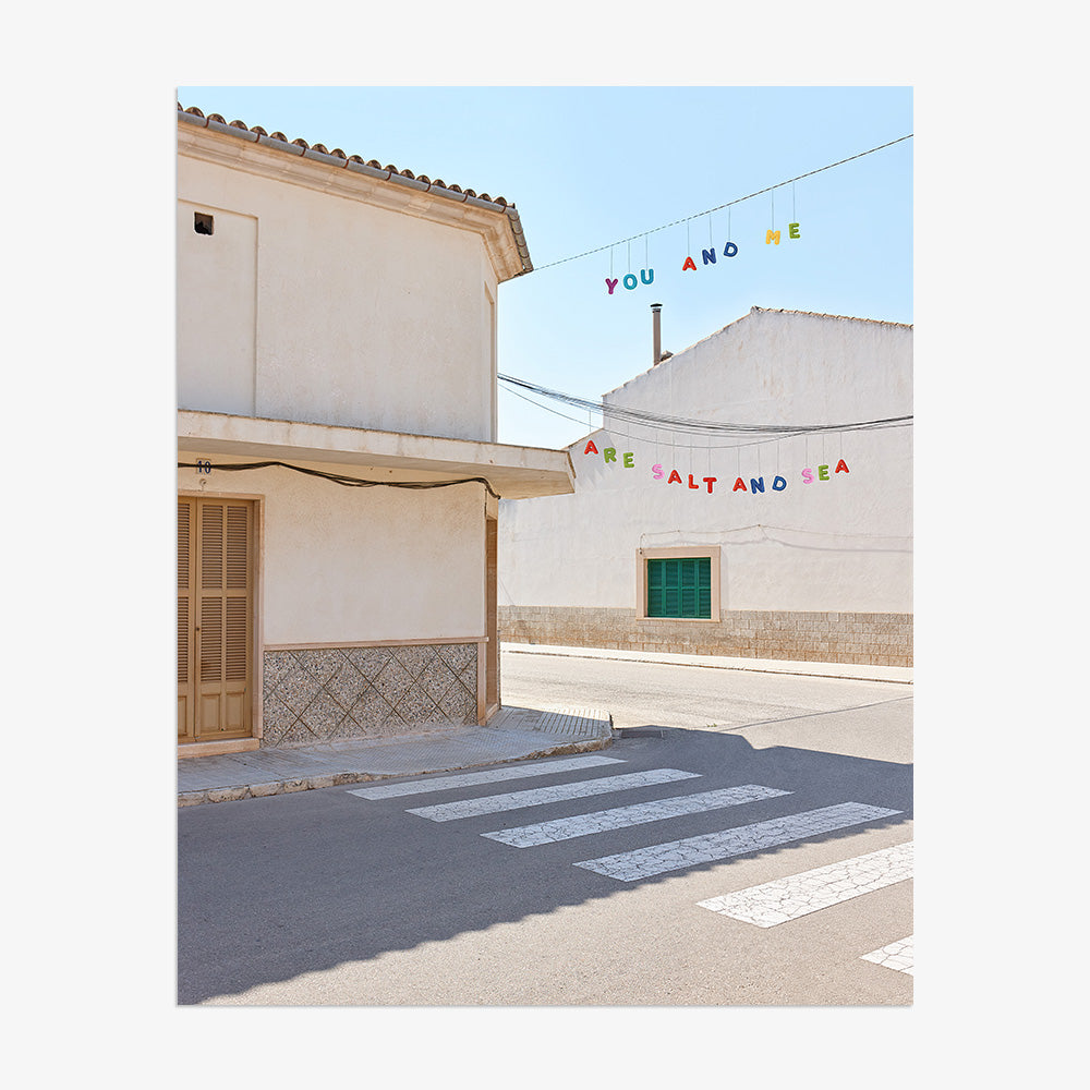 Street scene with white buildings a crosswalk and colorful hanging text presented without a frame