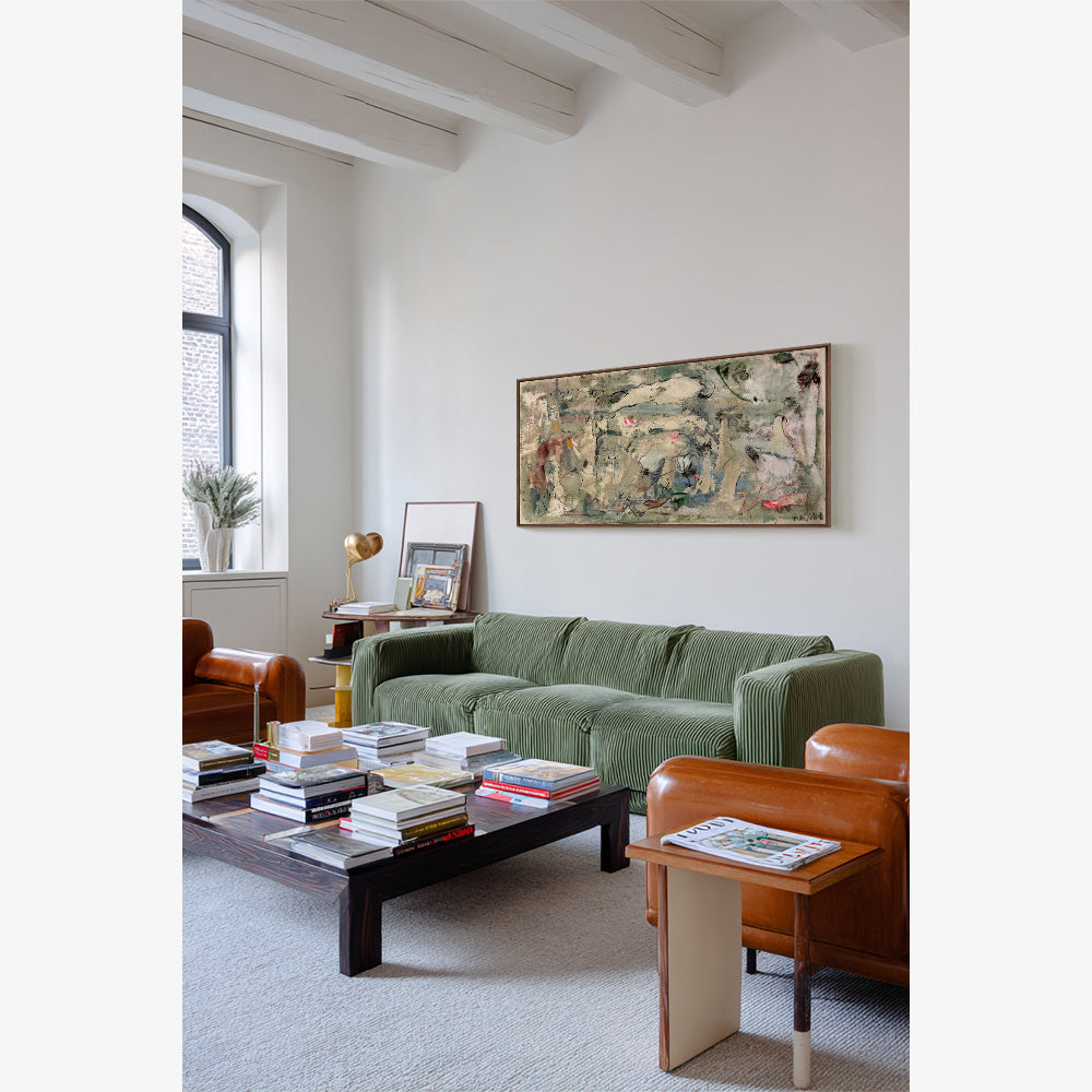 Framed abstract painting with earthy tones hanging above a green corduroy sofa in a modern living room