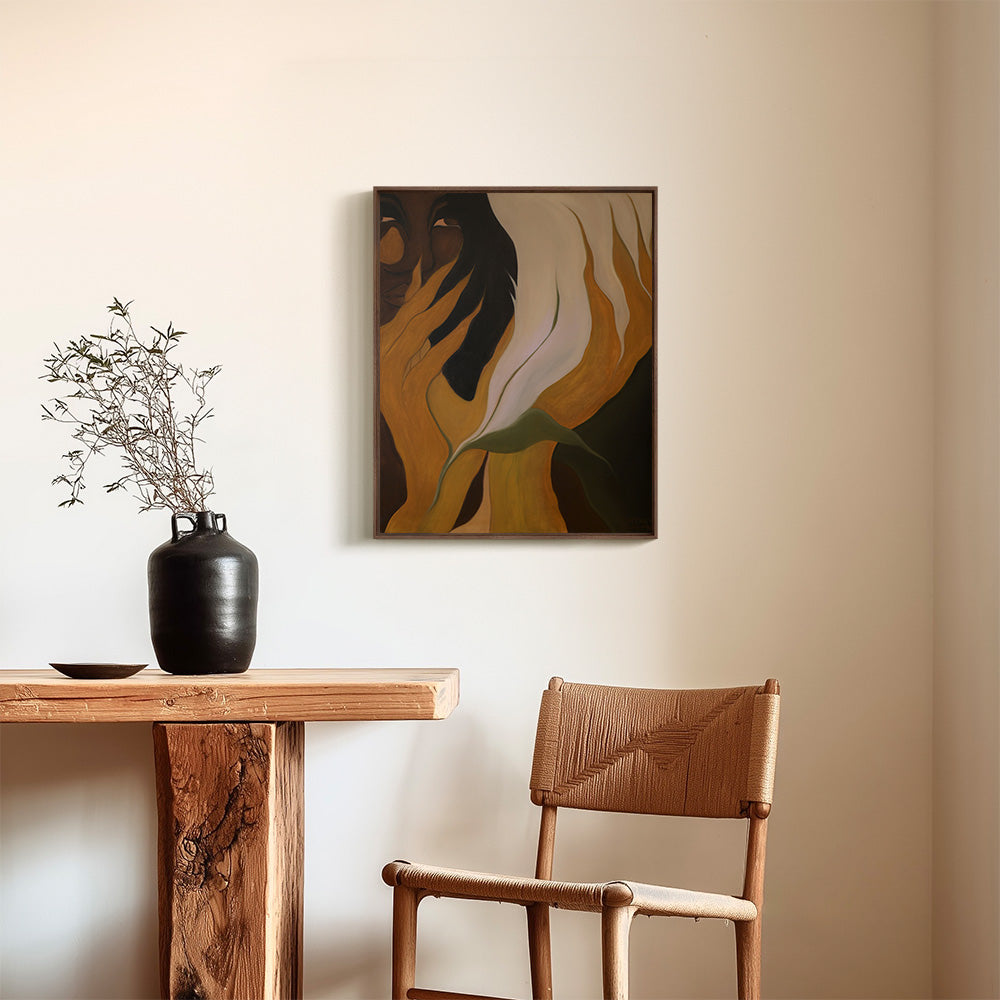 A framed abstract painting showing a face partially covered by stylized fingers hanging above a wooden table