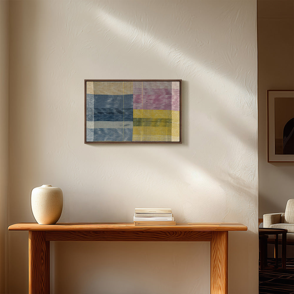 Textile artwork hanging on a neutral wall above a wooden console table with a vase and a stack of books