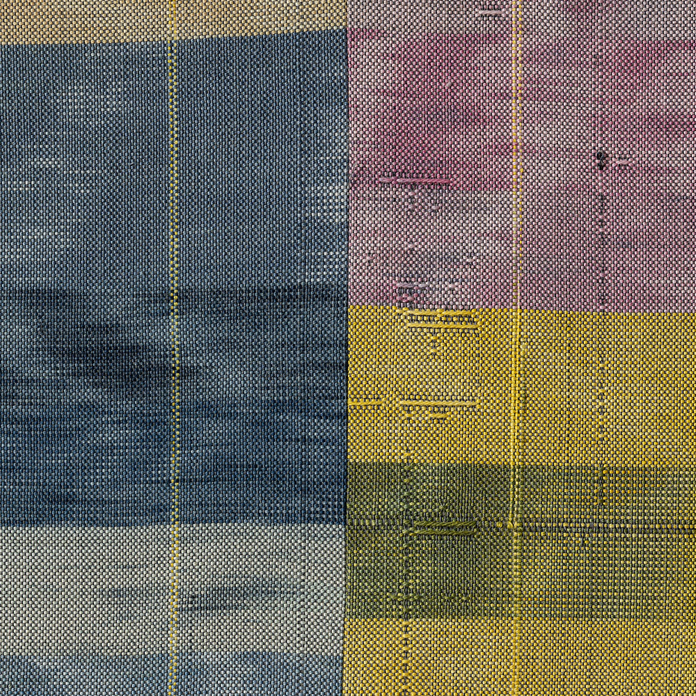 Close-up of a woven textile showing blue yellow and purple plaid sections with visible vertical and horizontal lines
