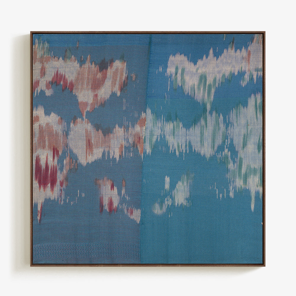 Abstract textile wall art in a dark wood frame with a soft cloud-like composition in shades of blue and muted red