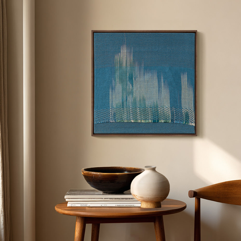 Textile art with blue hues and vertical light streaks hanging in a room with a wooden table bowl and vase
