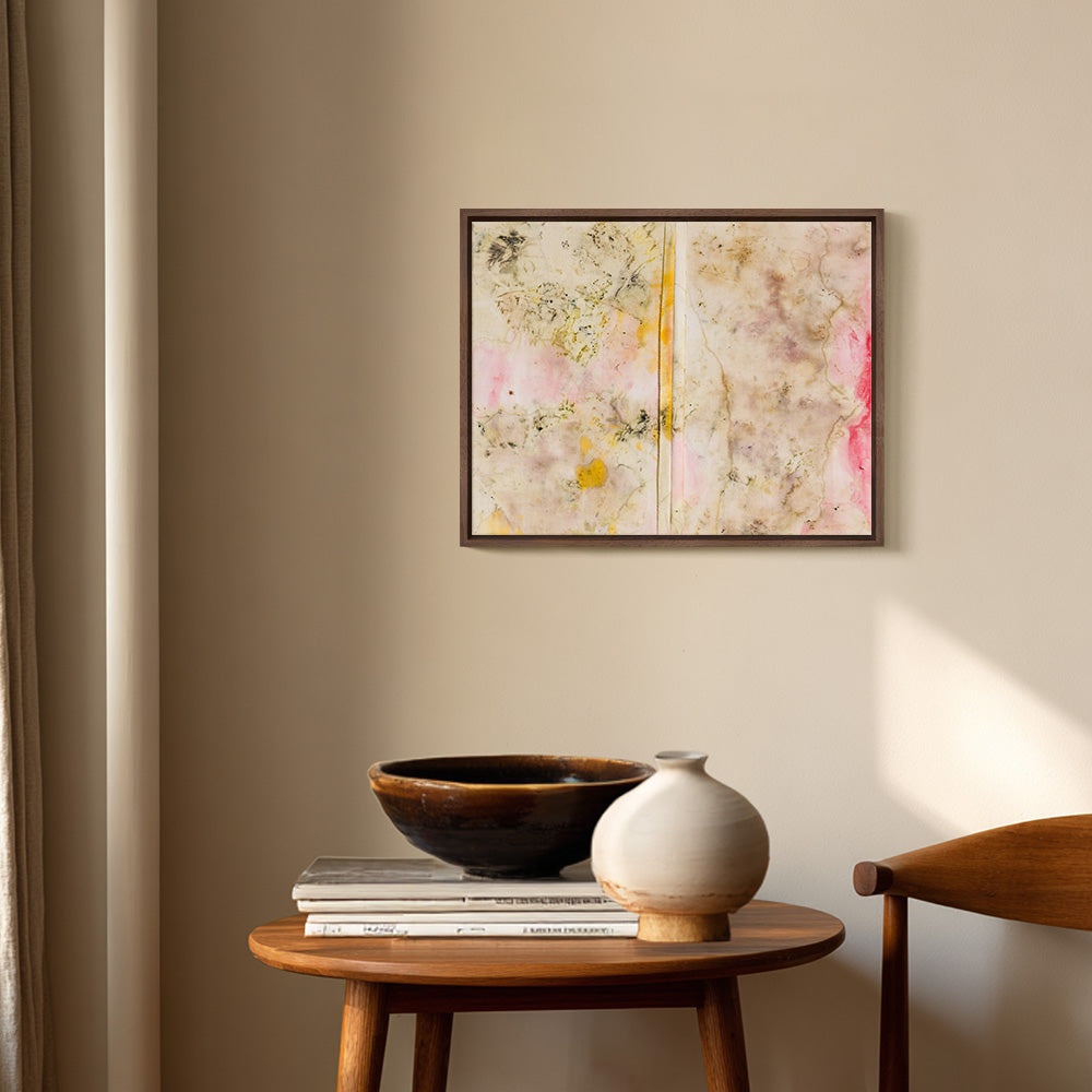 Framed textile art hanging above a side table with a ceramic bowl a vase and a stack of books
