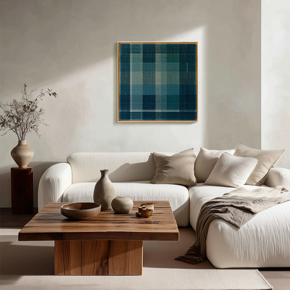 A square textile art in blue and white plaid hangs above a cream sectional sofa and wood coffee table in a modern