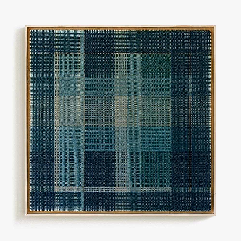 Square textile art in a light wood frame with an intricate plaid pattern in various shades of blue and white